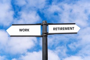 road sign that points to "work" in one direction and "retirement" in the other, with blue sky and clouds in background